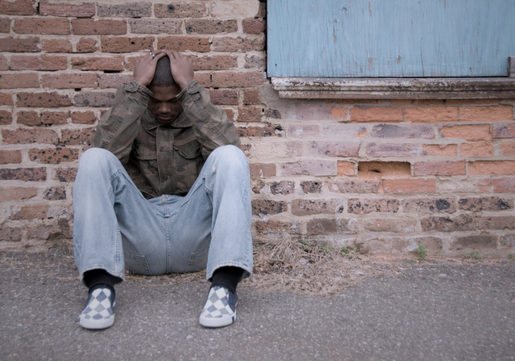 man sitting on the ground against the wall with his hands on his head
